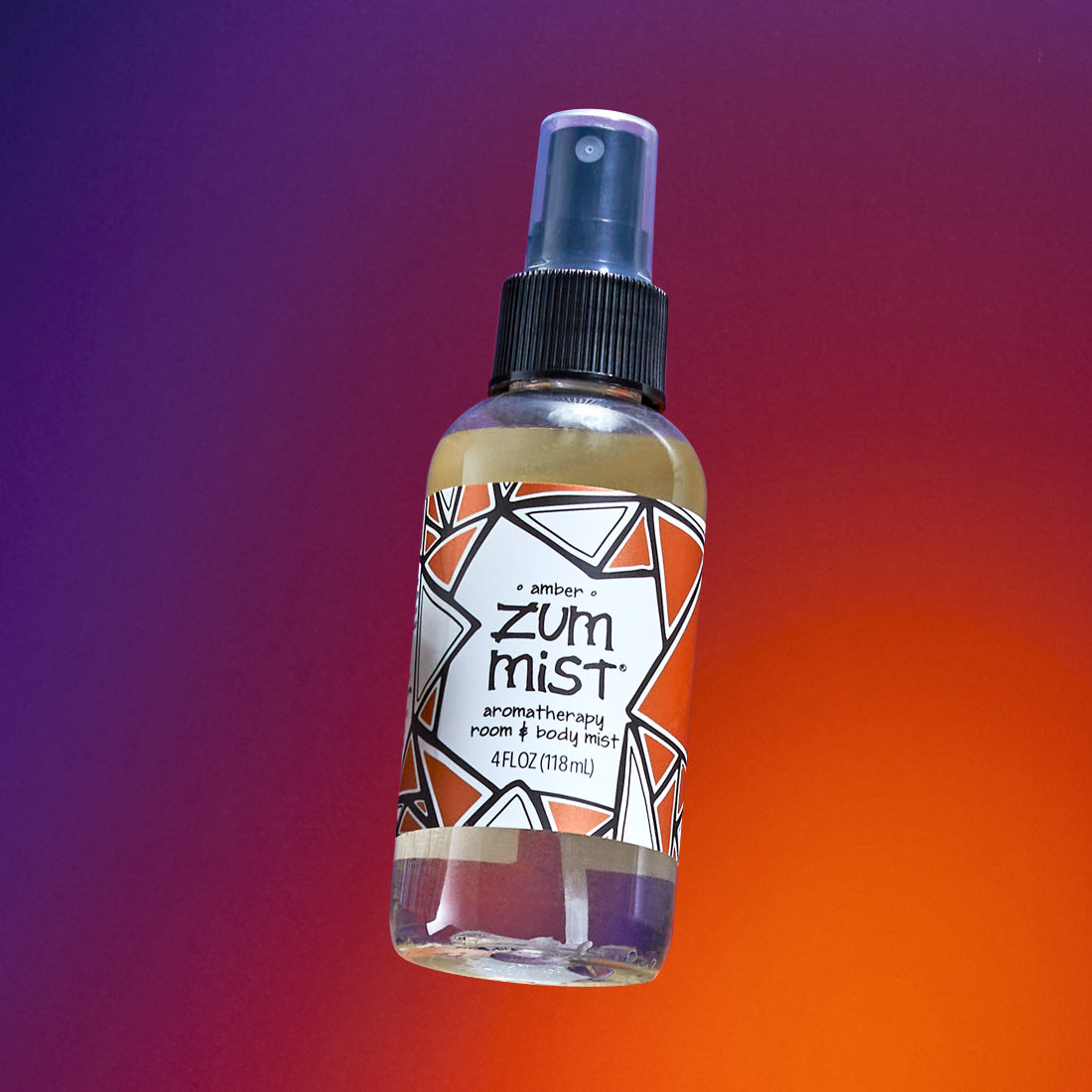 Labeled Amber scented Zum Mist bottle with a sprayer flying in the air. Purple to orange gradient background.