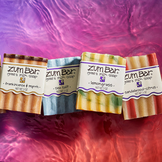 Frankincense & Myrrh, Sea Salt, Lemongrass, and Sandalwood-Citrus labeled bar soaps lined up on a watered surface. Purple to orange gradient background.