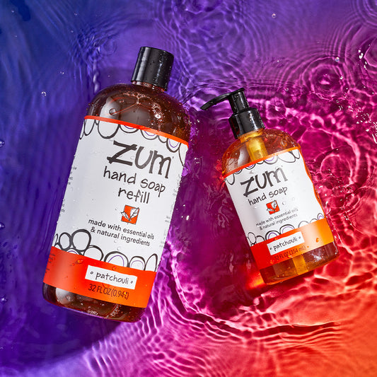 Patchouli 32 fl oz bottled hand soap and Patchouli 12 fl oz bottled hand soap laying on a watered surface. purple to orange gradient background