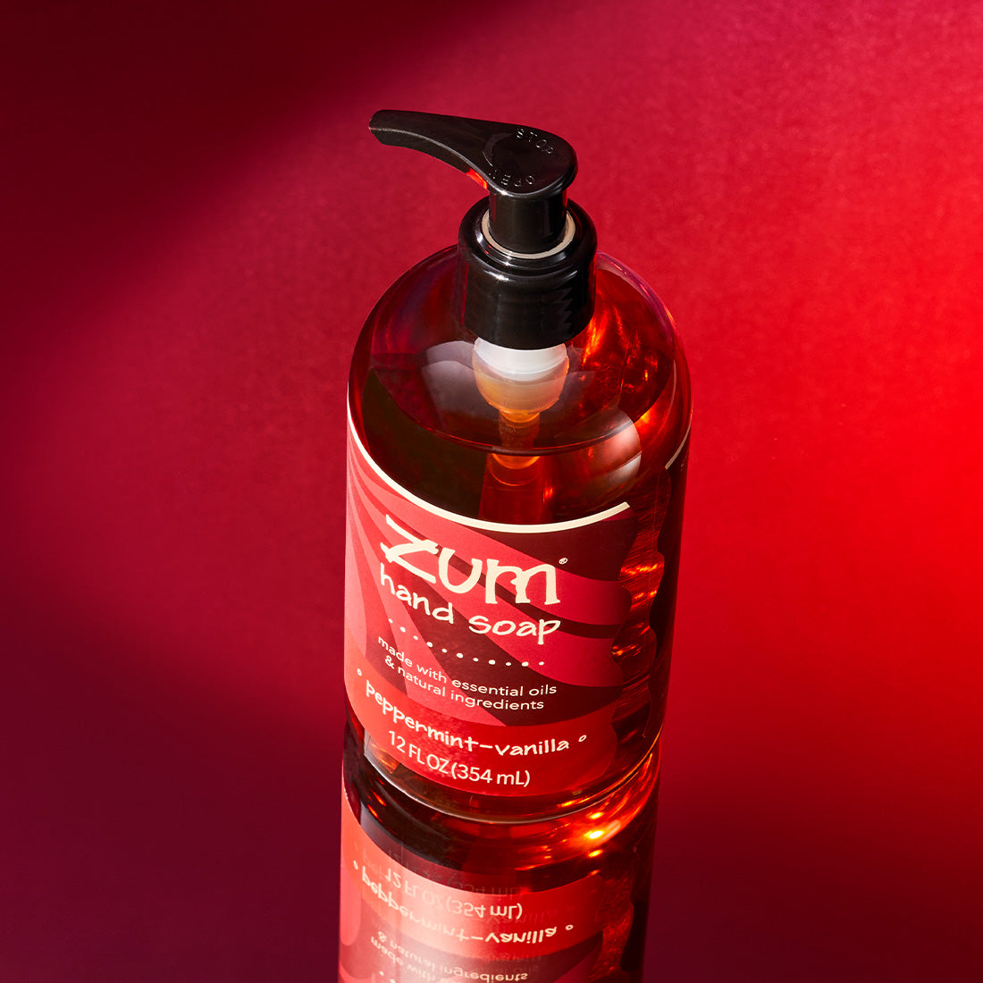 Birds eye view shot of Peppermint-Vanilla hand soap bottle with a pump on a mirrored surface with a dark red to bright red gradient background.