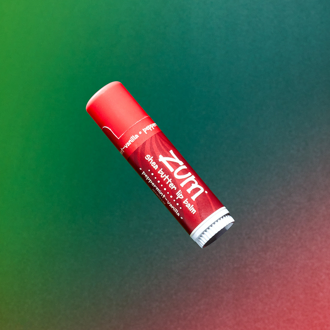 Peppermint-Vanilla flavored 0.5 oz Lip Balm tube flying in the air with a green to red gradient background.