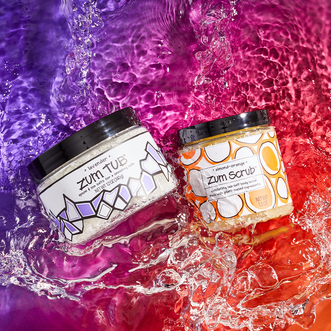 Jarred lavender epsom and sea salt bath salts and almond-orange sea salt body scrub in splashing water. Purple to orange background.