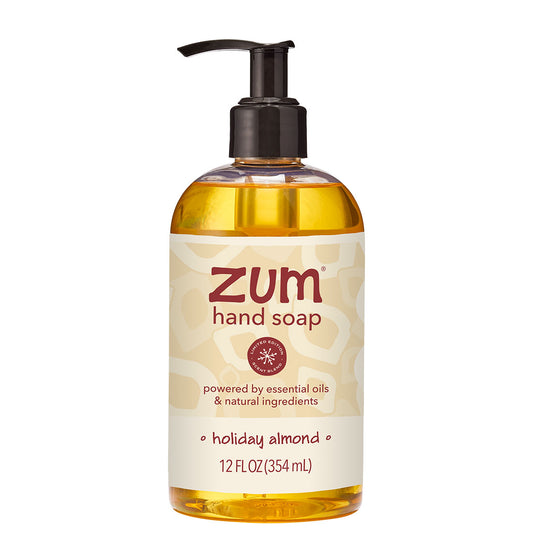 A 12 fl oz bottle of Zum Hand Soap in the Holiday Almond scent, featuring a clear bottle filled with golden-yellow liquid, a black pump dispenser, and a cream-colored label with red and brown text.