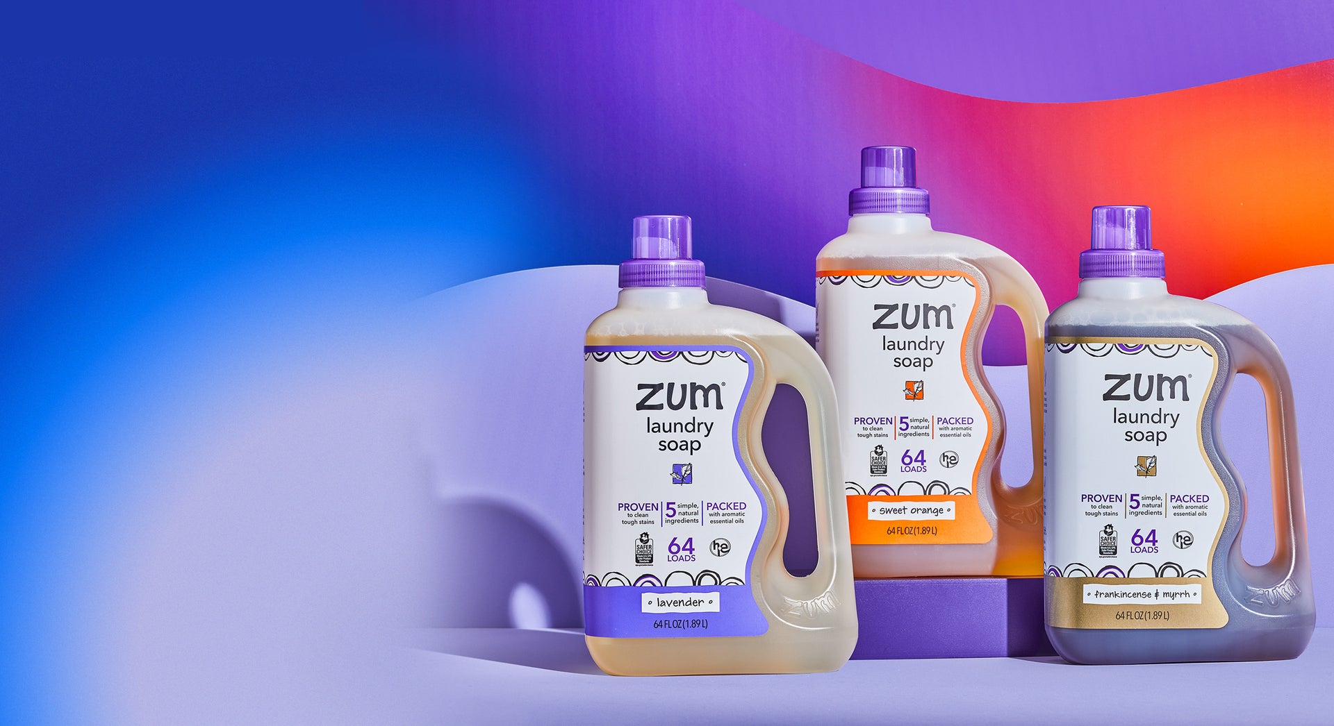 Lavender, Sweet-Orange, and Frankincense & Myrrh bottles of laundry soap on a light purple surface with wavy gradient.